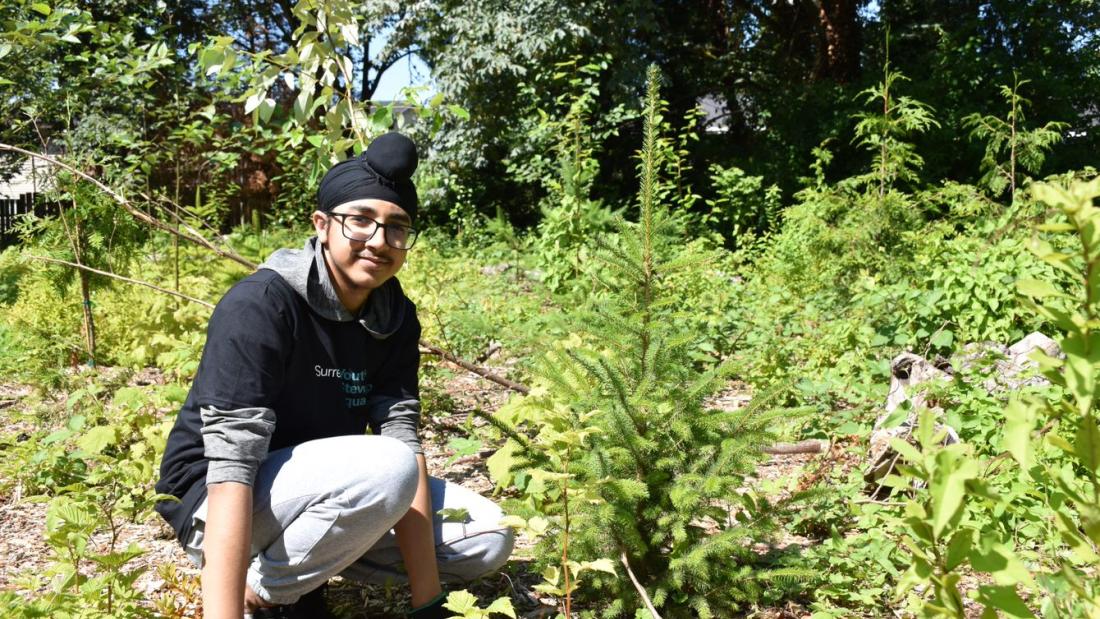 Youth volunteer next to tree.