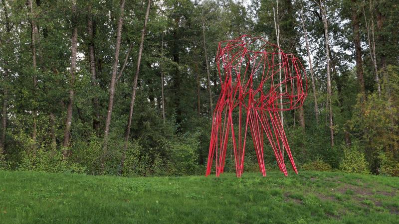 A large red metal sculpture in a wooded greenspace 
