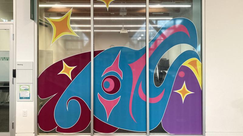 A representation of a Thunderbird in Salish culture using bright colours that fill the windows of a meeting room.