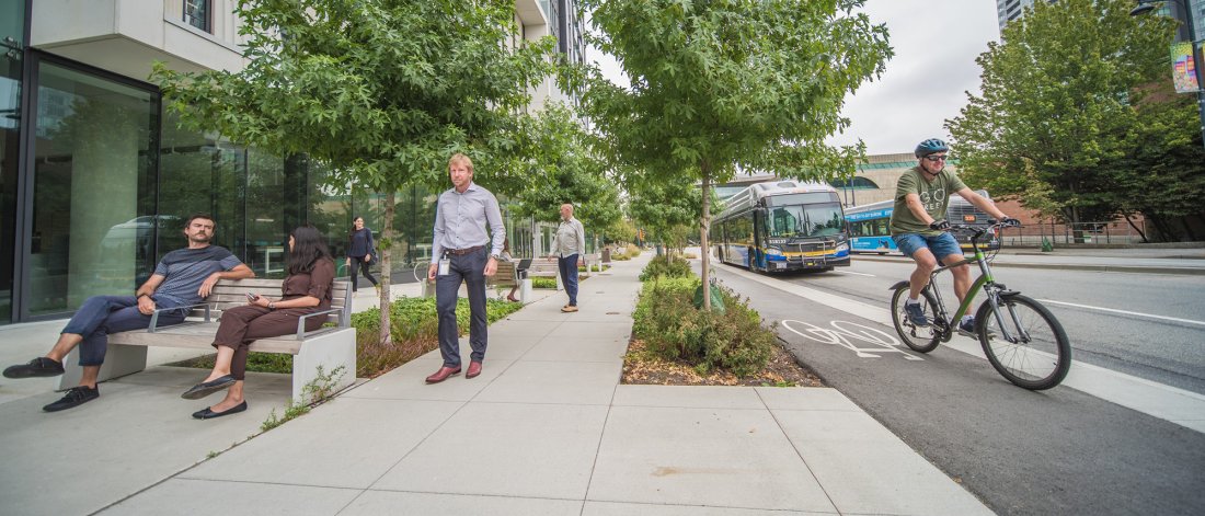 pedestrian walking next to a cyclist with a bus in the background
