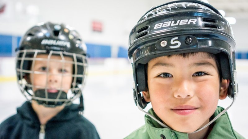 Two kids smiling with hockey helmets on.
