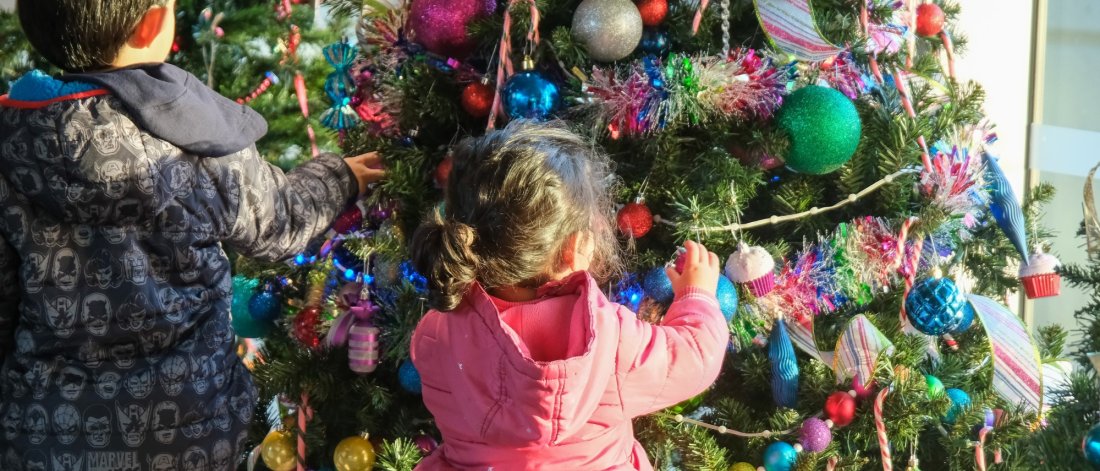 Two young children decorating a Christmas tree with colorful ornaments and tinsel.