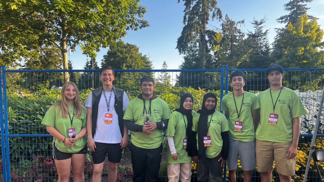 The Youth Event Squad lined up against a garden and blue fence. All YES members are wearing a green volunteer shirt.