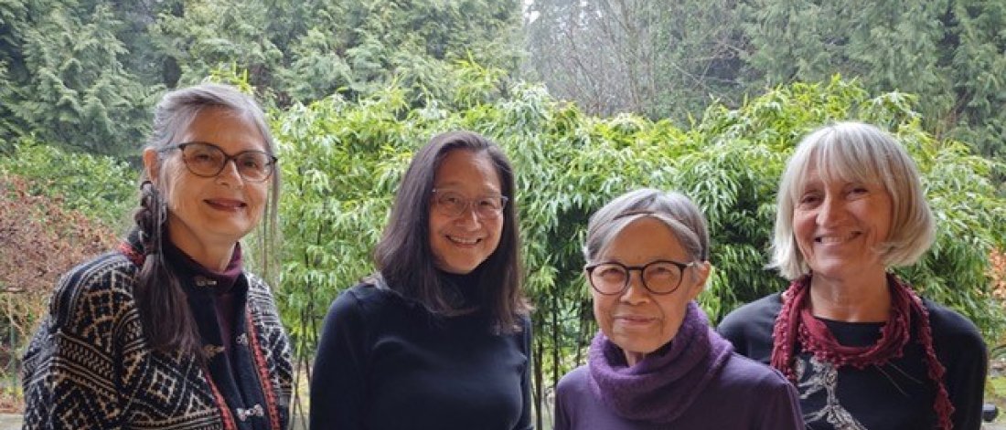 Four women face the camera and smile against a lush garden setting.