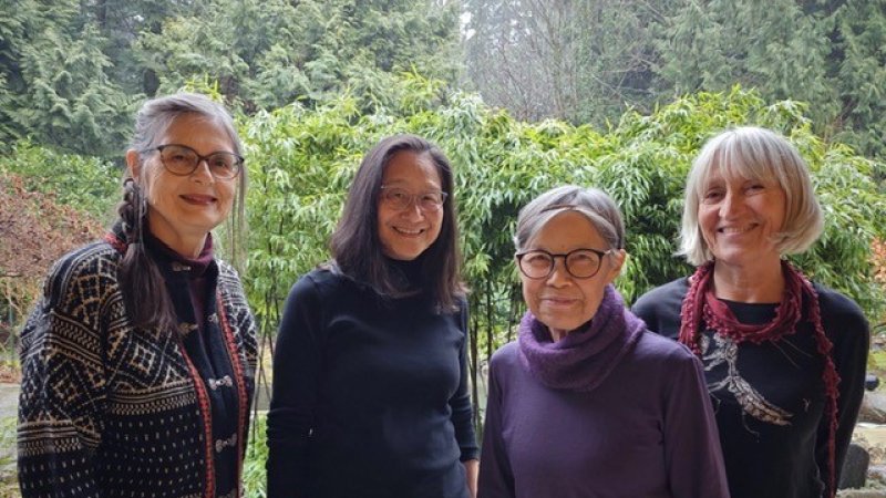 Four women face the camera and smile against a lush garden setting.