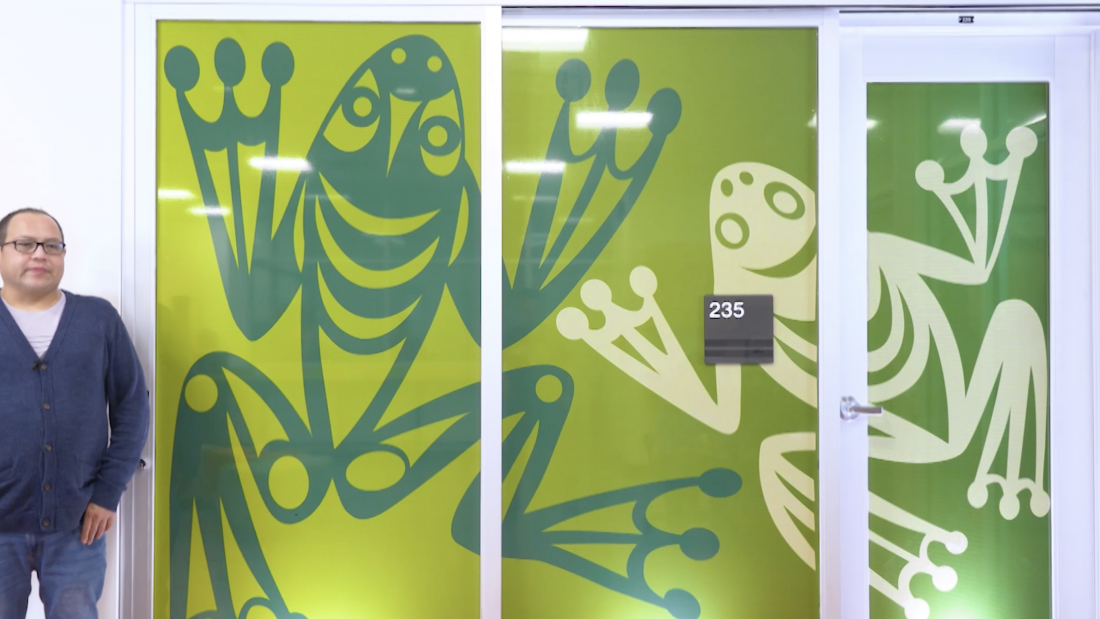 Brandon Gabriel next to his artwork of green jumping frogs