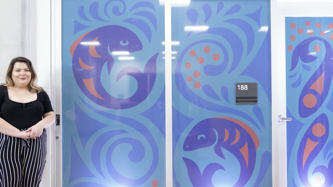 Elinor Atkins standing beside Coast Salish artwork of swimming salmon 