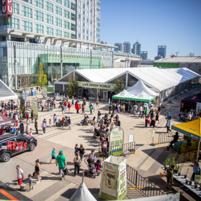 An outdoor event with tents, crowds, and city buildings in the background on a sunny day.