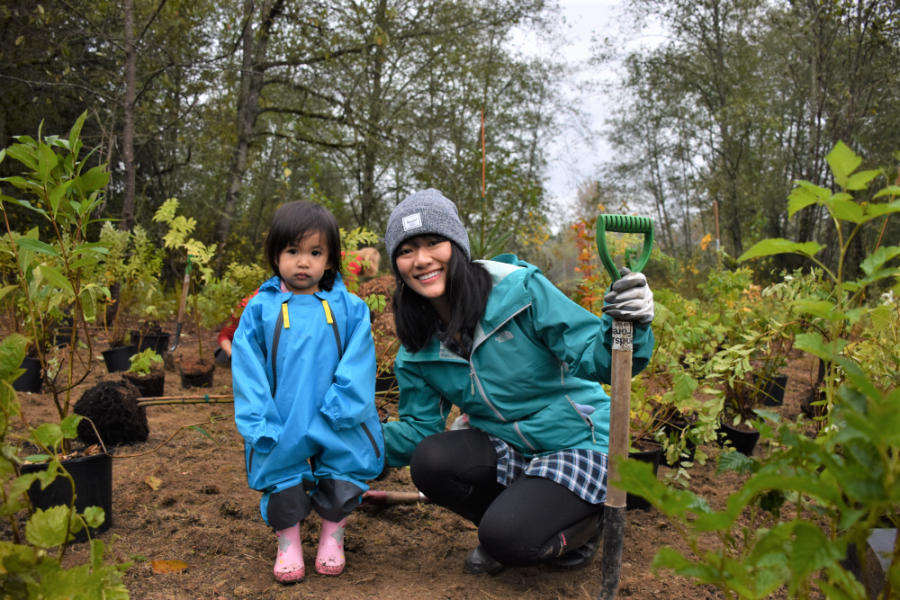 A mother crouching next to her daughter at a tree planting event.