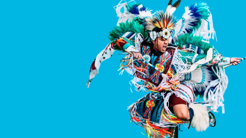 Dancer Notorious Cree aka James Jones in full colourful regalia on a bright light blue background